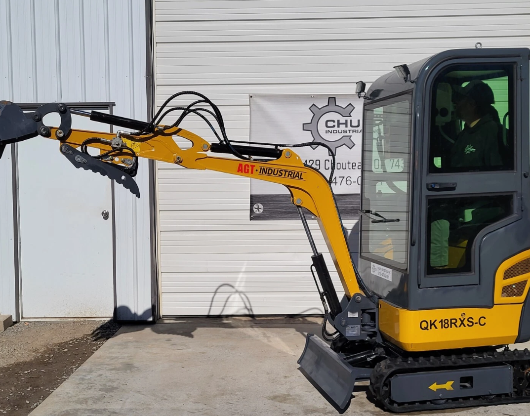 QK18RXS-C boom fully extended with the hydraulic thumb open, operator seated in the enclosed cab
