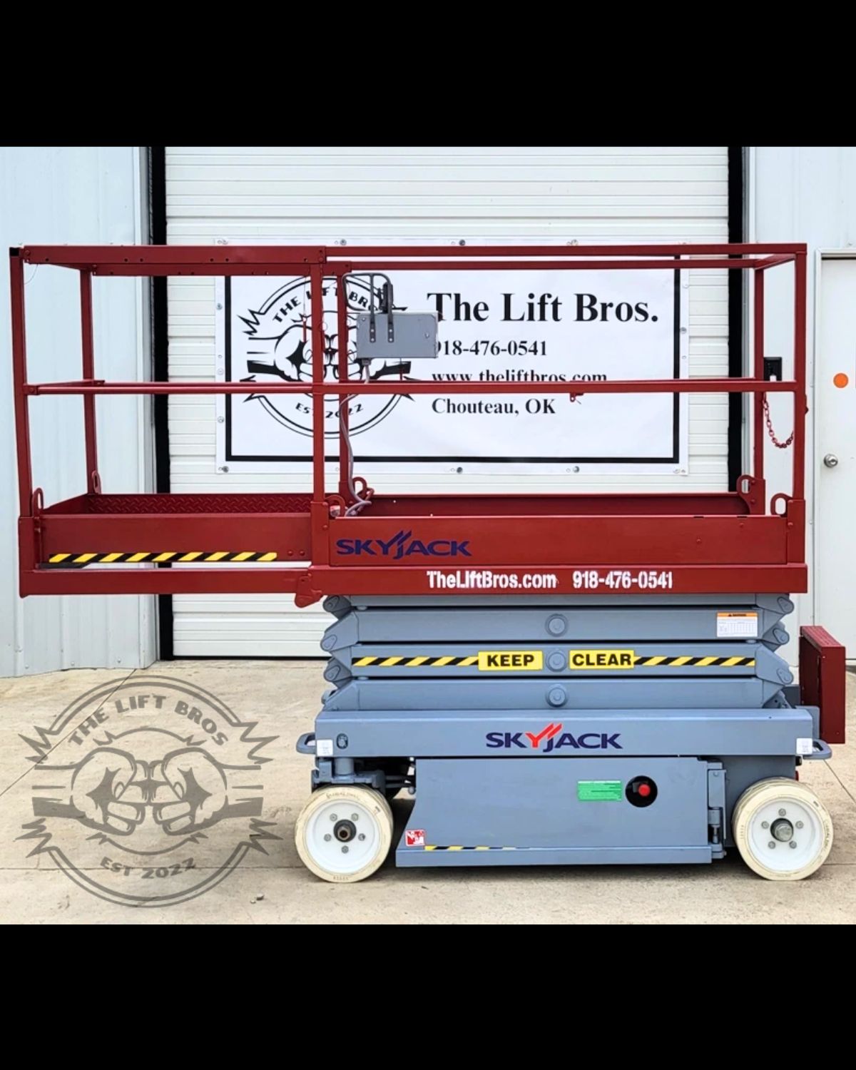Skyjack scissor lift lowered, red platform deck overhanging the gray chassis on white non-marking tires