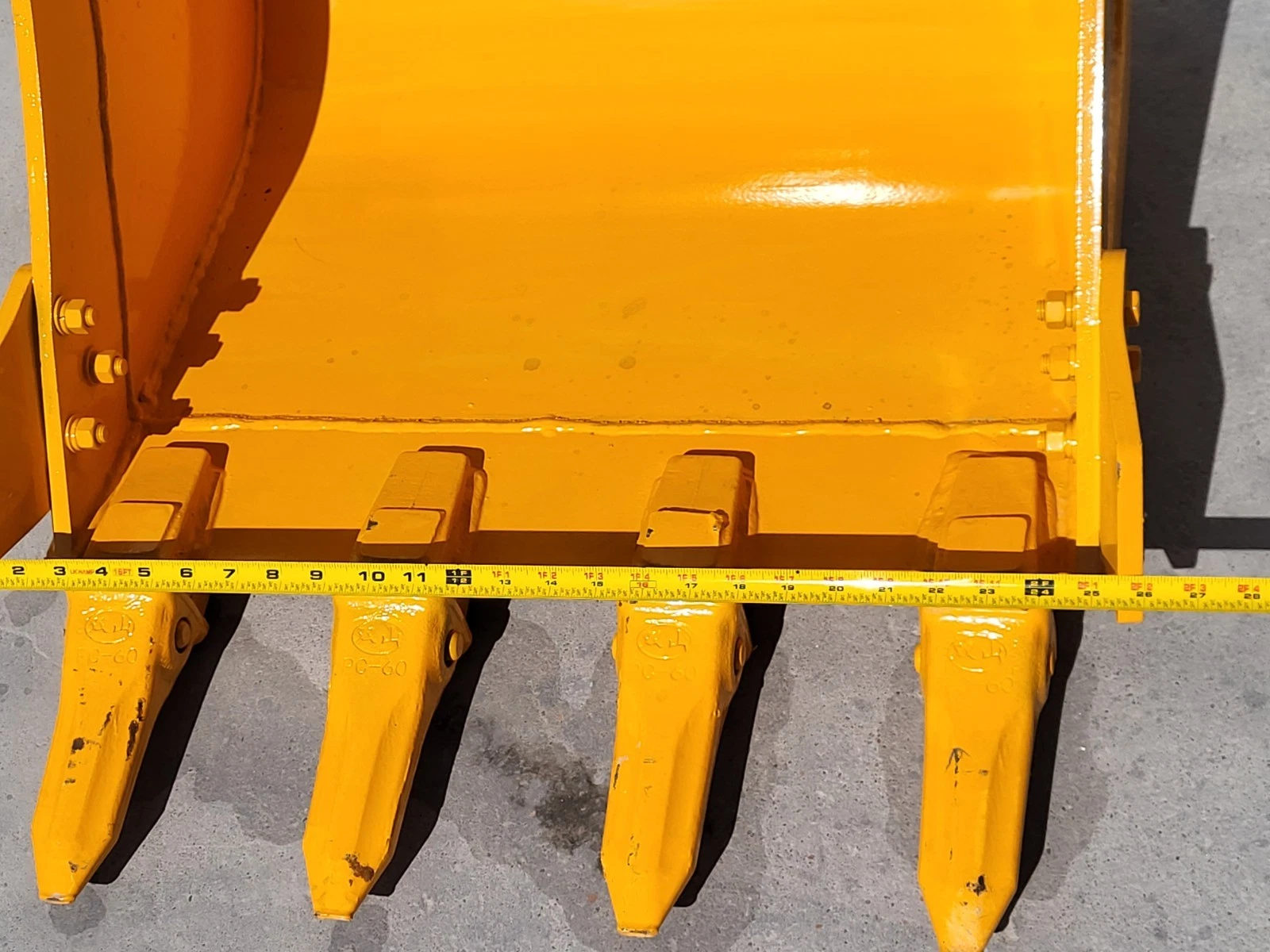 Tape measure across the yellow bucket's cutting edge, four teeth cast PC-60 hanging below