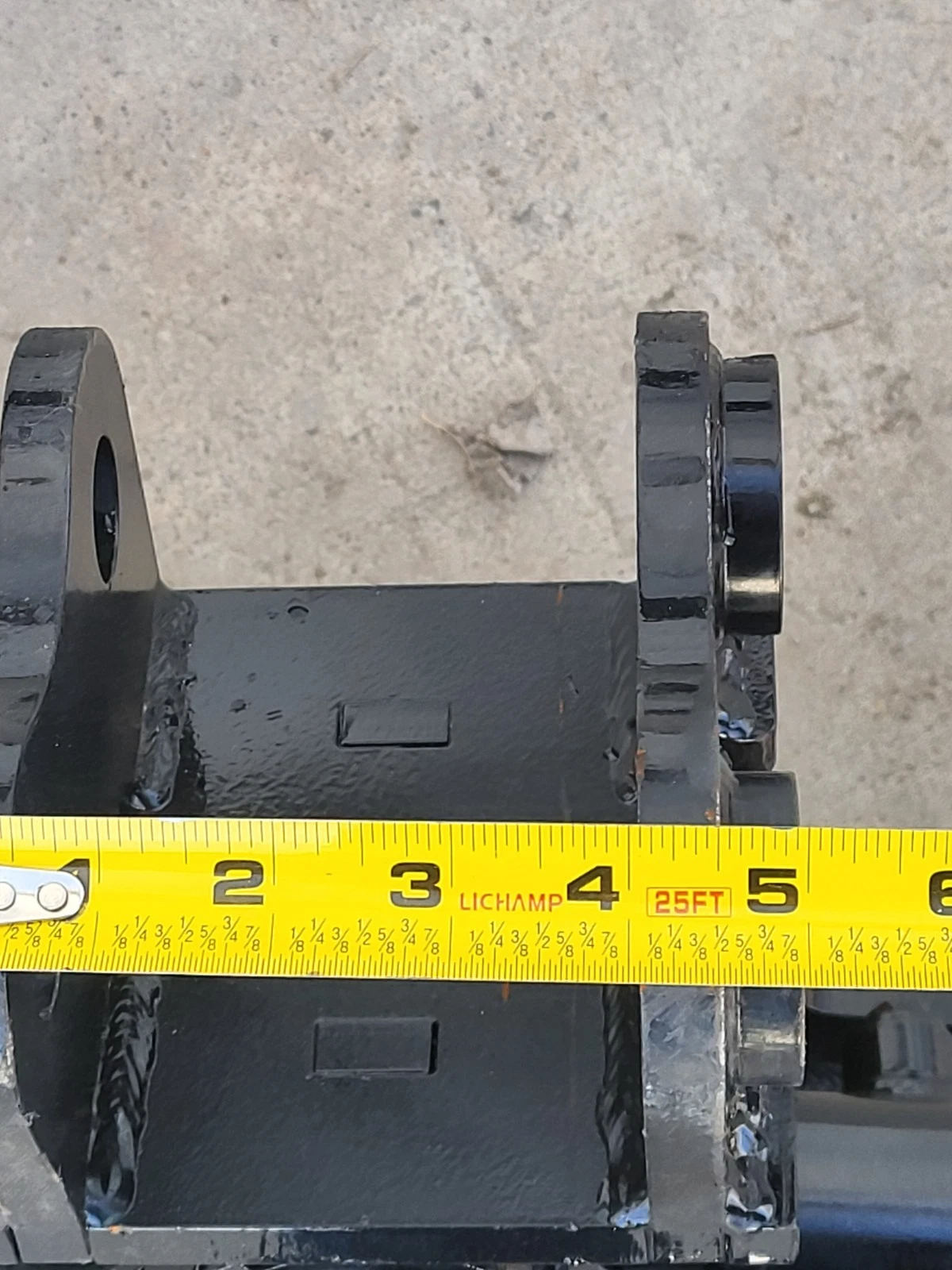 Tape measure across the tilt bucket's mounting bracket pin ears, spanning about 5 inches