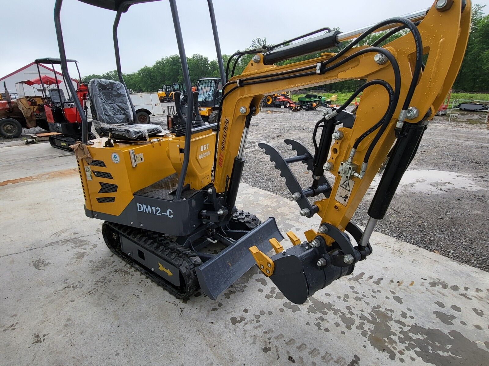 AGT DM12-C mini excavator from the rear: canopy, wrapped seat, boom out with the hydraulic thumb open above the bucket
