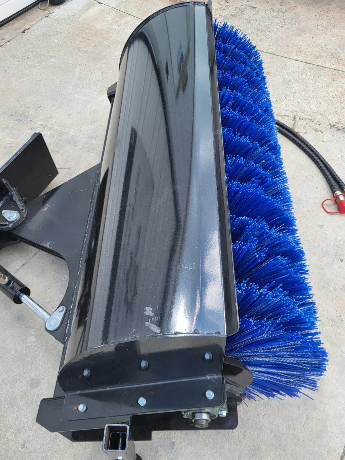 Angle broom from above: black hood over the blue bristle roller with the angle cylinder at the mount