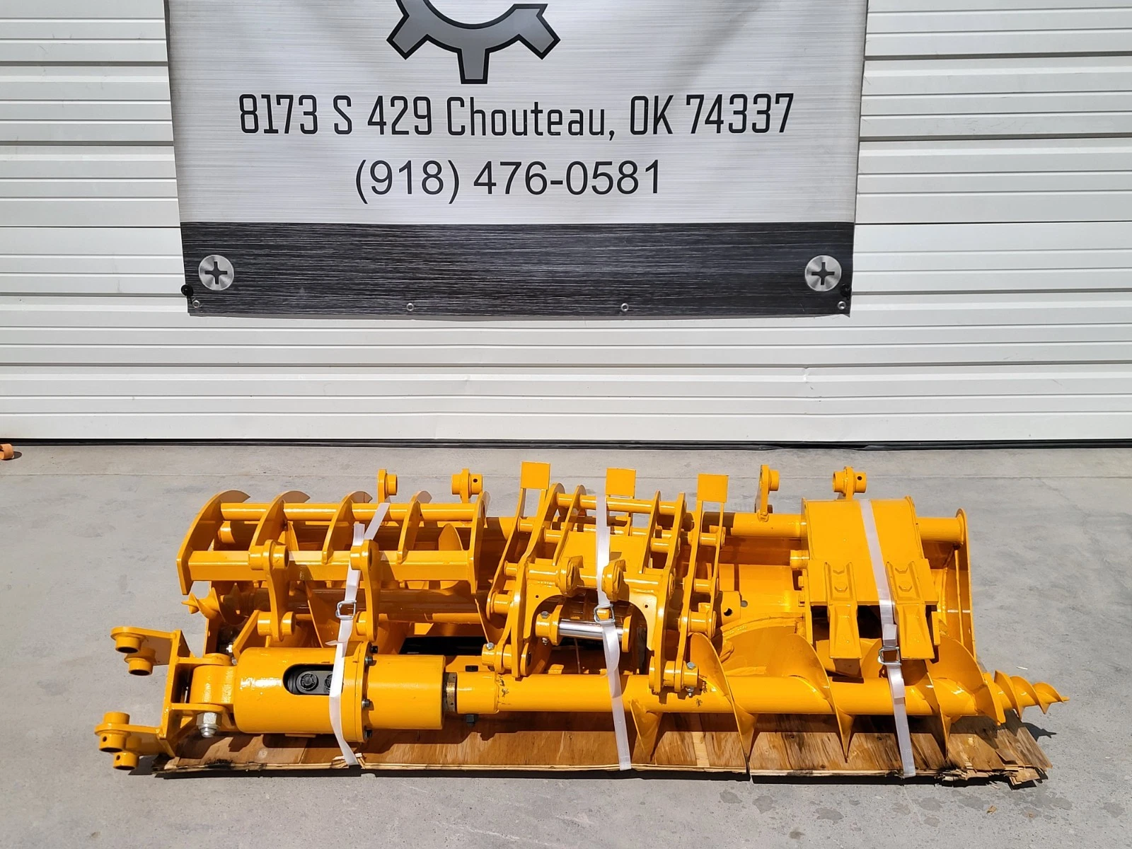 Yellow attachment package on a pallet below the shop address banner: auger bit, cylinder and buckets