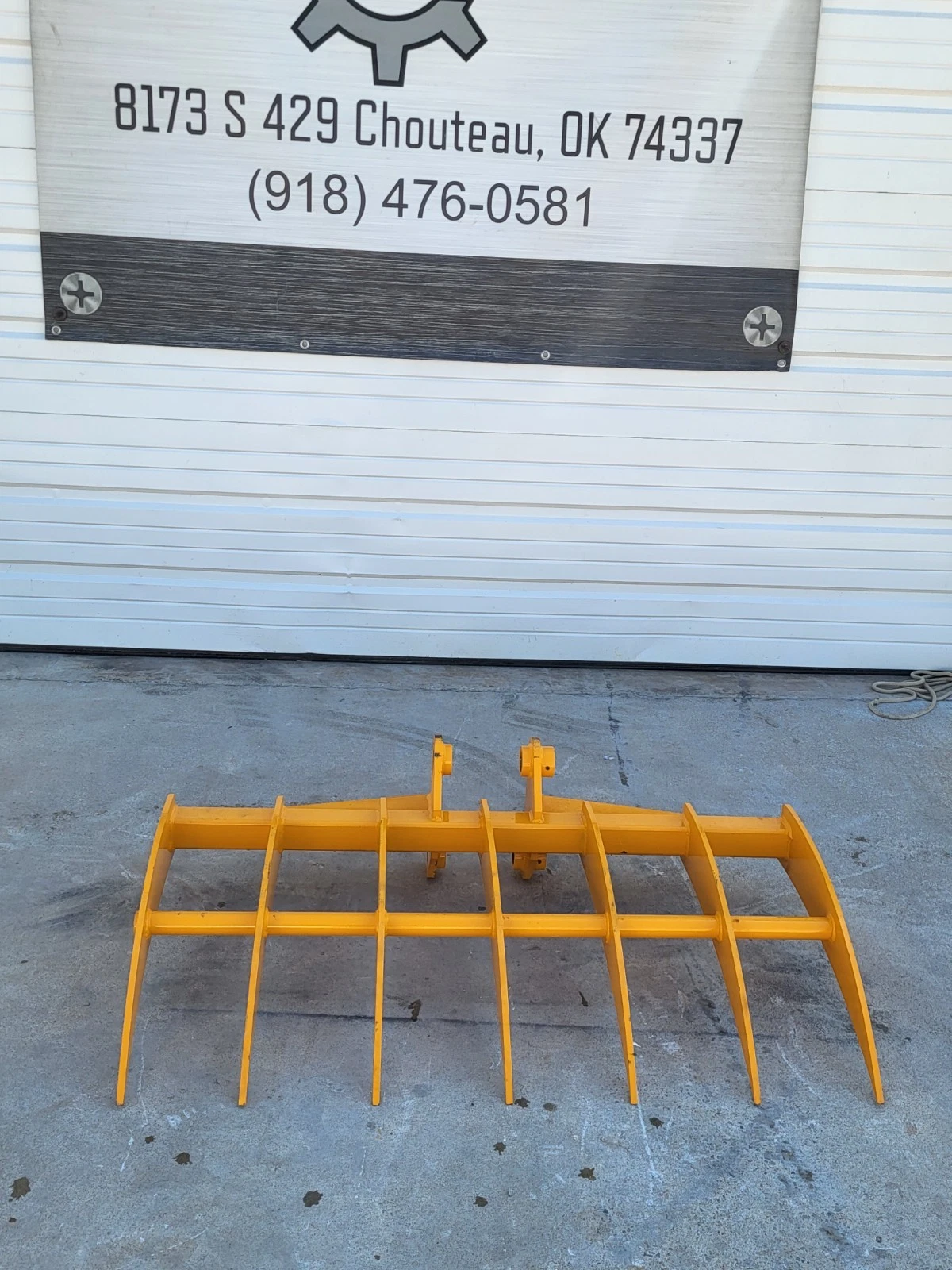 Yellow 46-inch excavator root rake, seven curved tines on a tubular frame with twin pin bosses