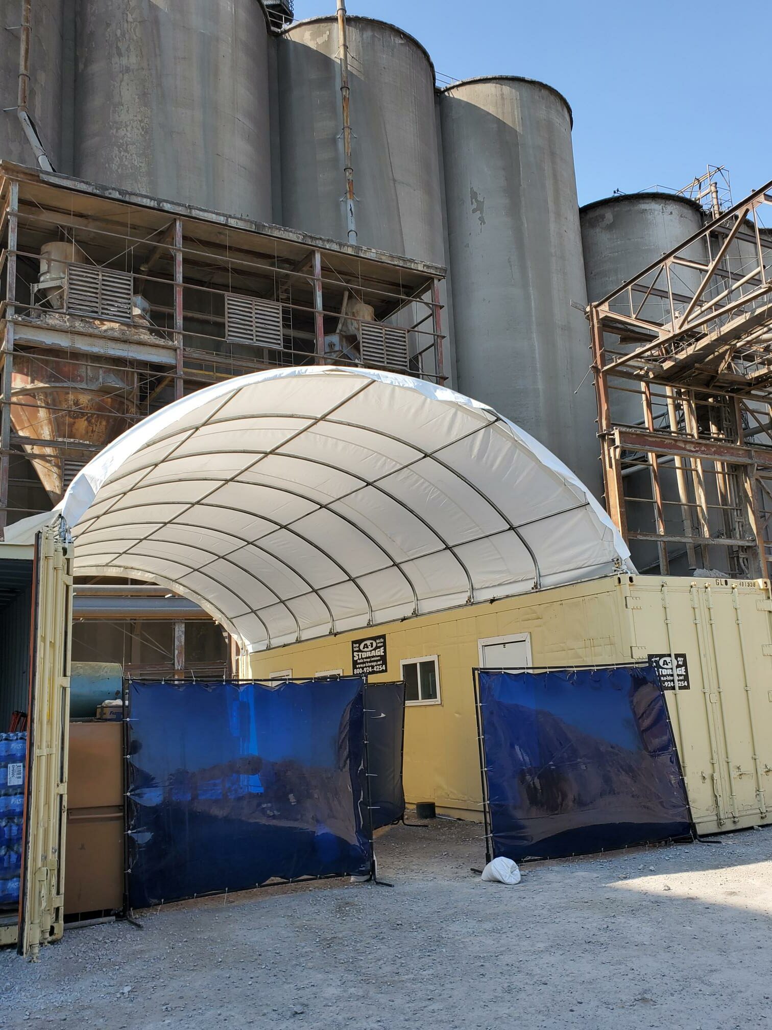 White PVC container shelter arched between two shipping containers on a galvanized steel frame