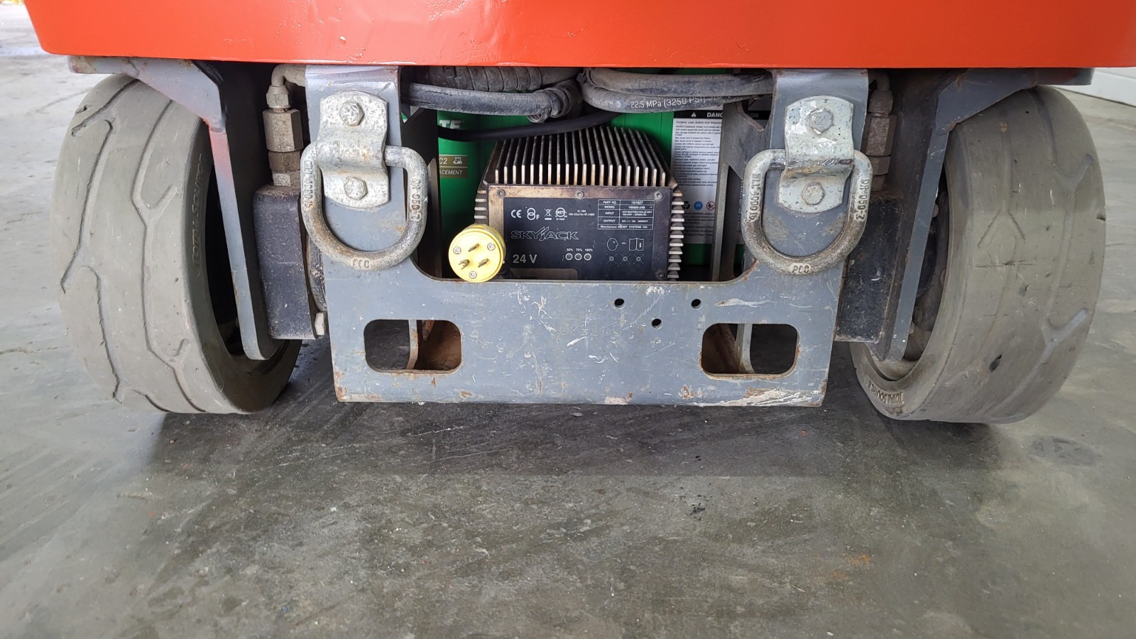 Underside of a Skyjack lift base, 24-volt battery charger, tie-down lugs and solid wheels