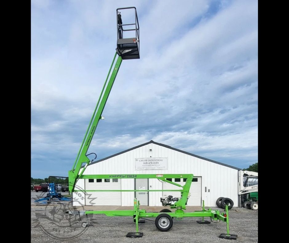 Green Nifty TM34 towable boom lift with the boom raised and work platform elevated on outriggers