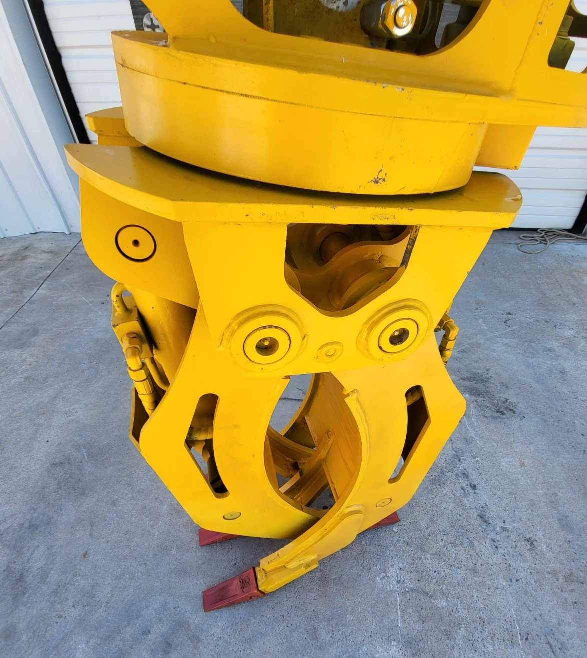 Grapple rotator bearing and mount plate above the curved yellow tines, red tooth tips at the base