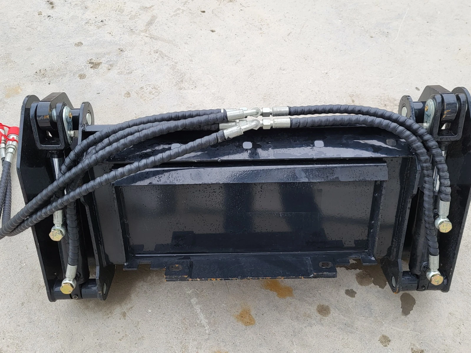 Black 4-in-1 mini skid steer bucket from the back: quick-attach mount plate, braided hoses and couplers