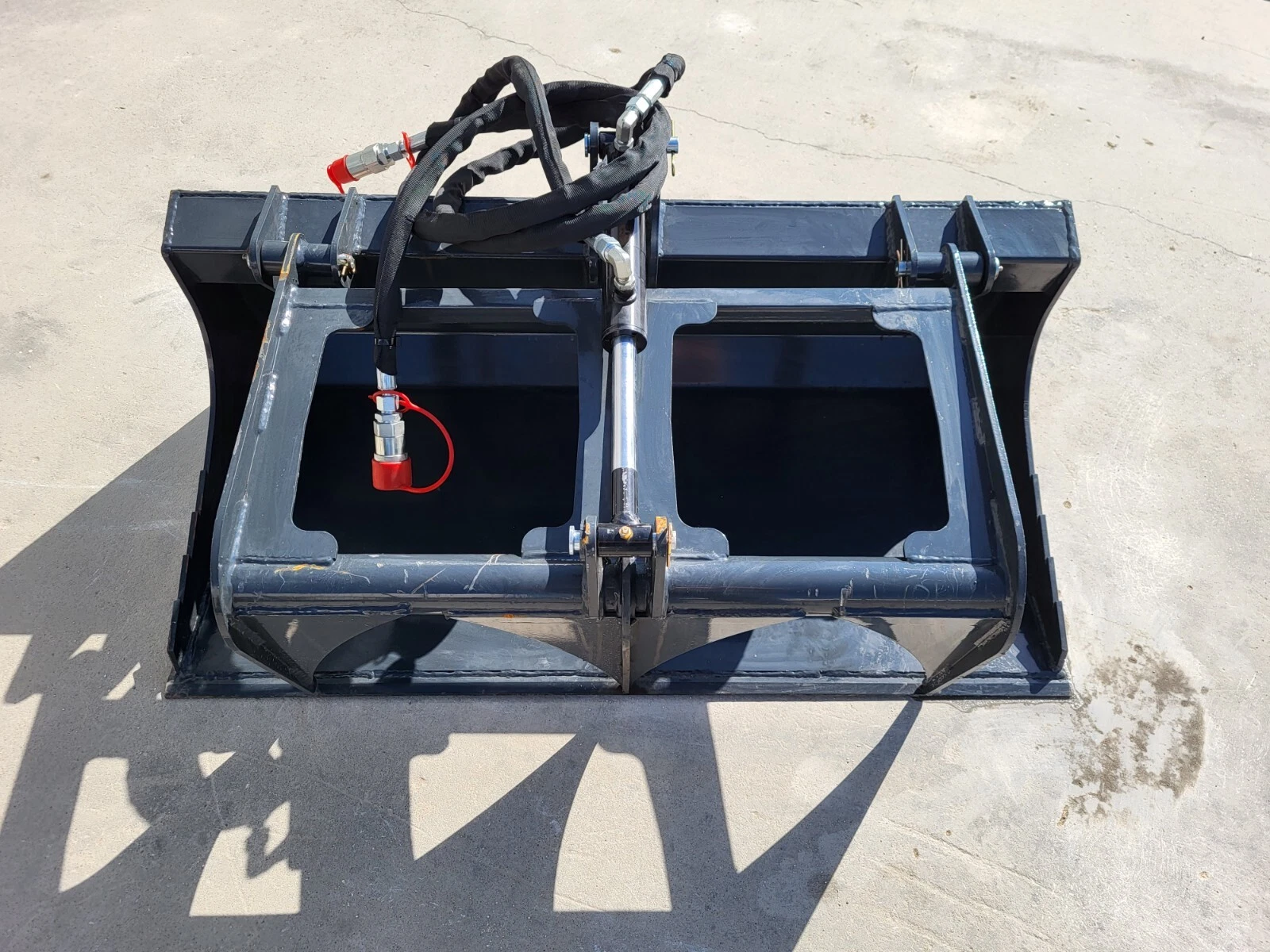 Grapple bucket from above: one hydraulic cylinder centered between the grapple arms, red-capped coupler