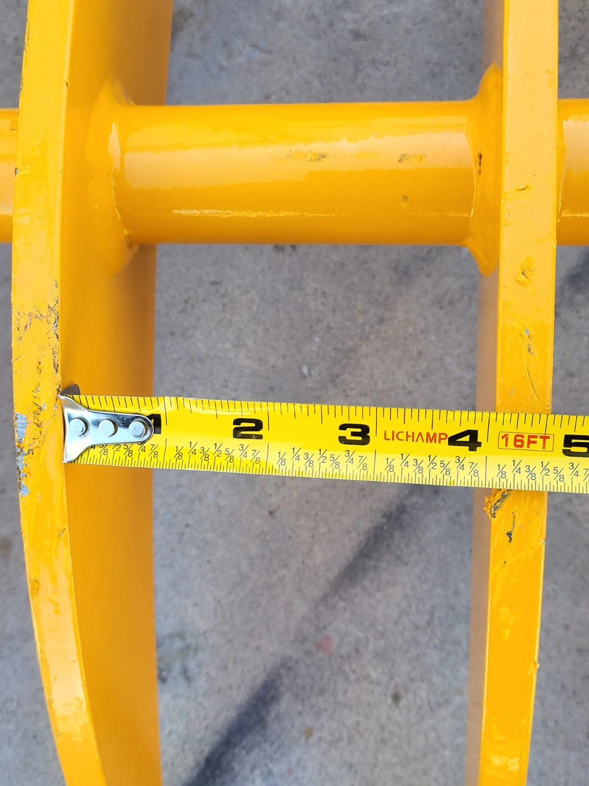 Tape measure across the gap between two of the yellow rake's tines, spanning about four inches