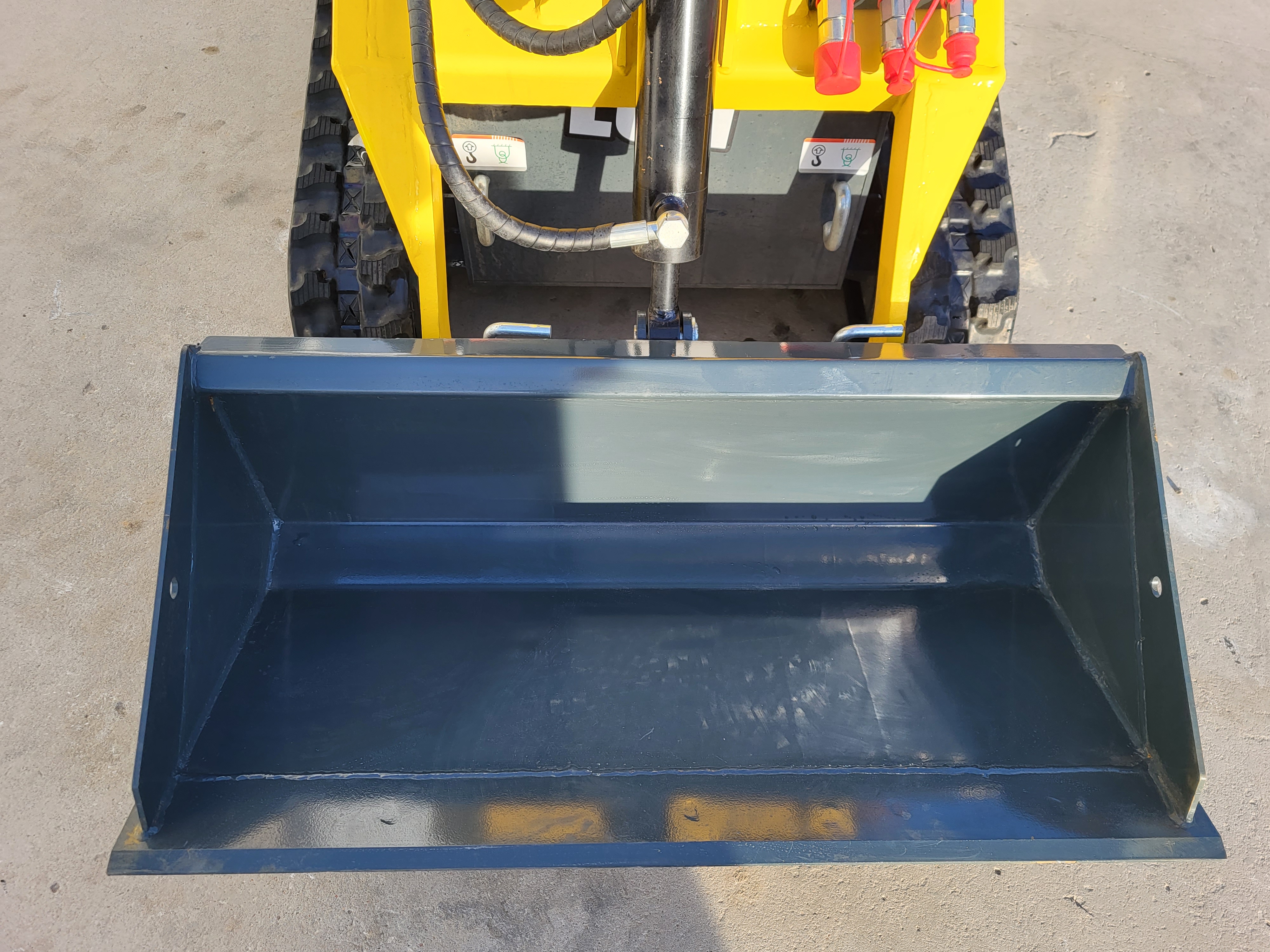 EG360 wide black dirt bucket lowered flat, with the loader arms and red-capped hydraulic couplers behind