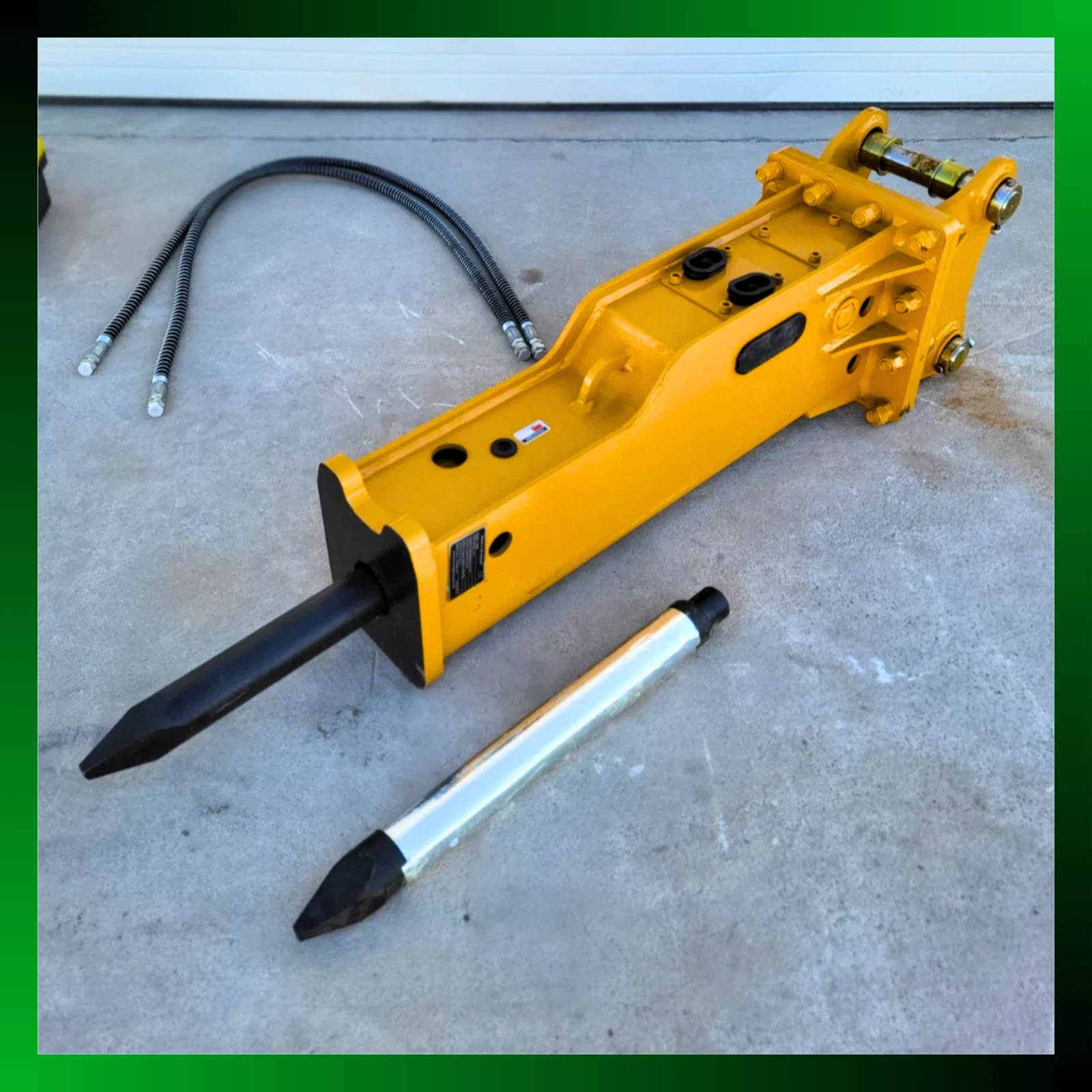 Yellow SB45 hydraulic breaker at an angle, black moil chisel fitted, spare chrome chisel and two hydraulic hoses