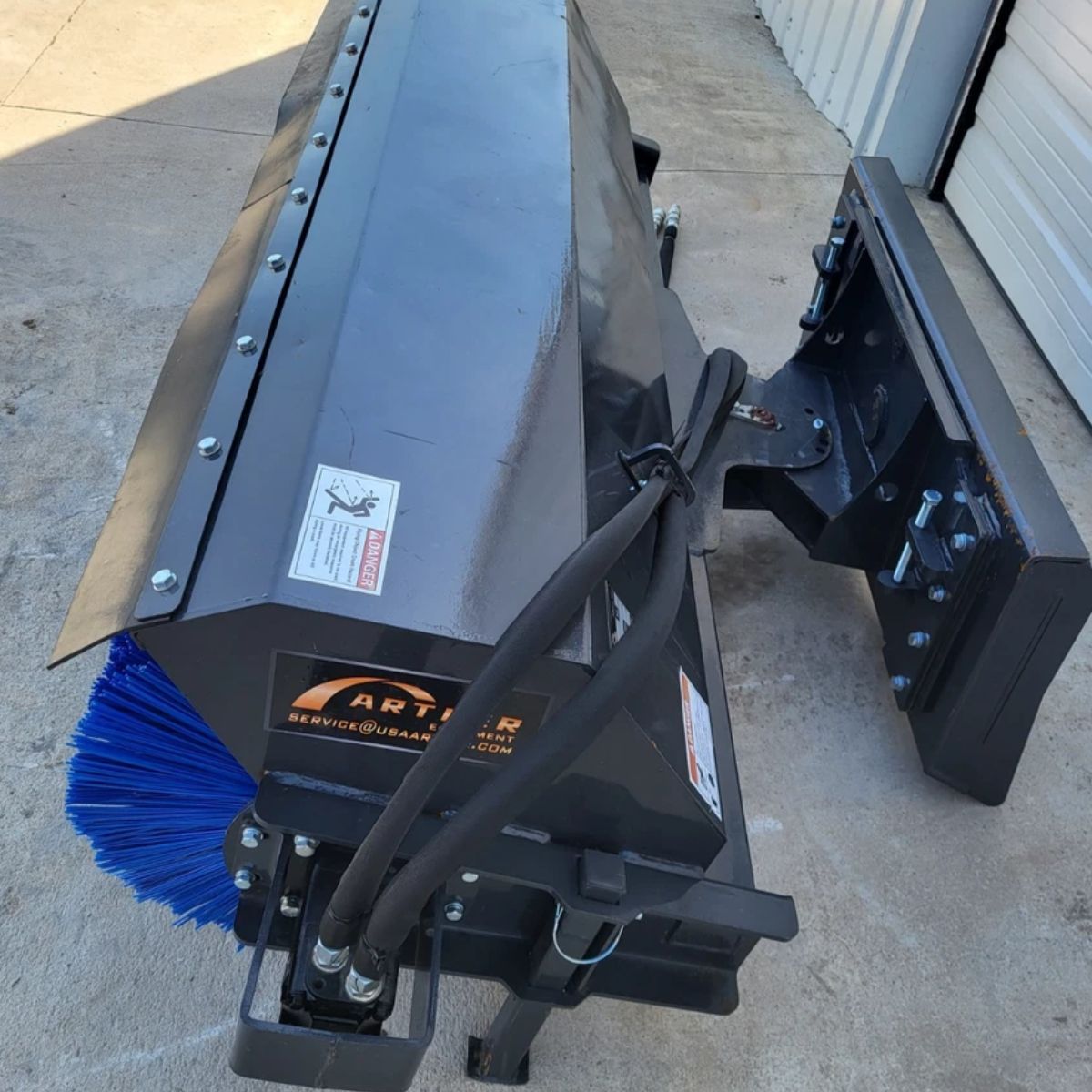 Arteer angle broom from above: steel hood, Arteer decal, hydraulic hoses and skid steer quick-attach plate