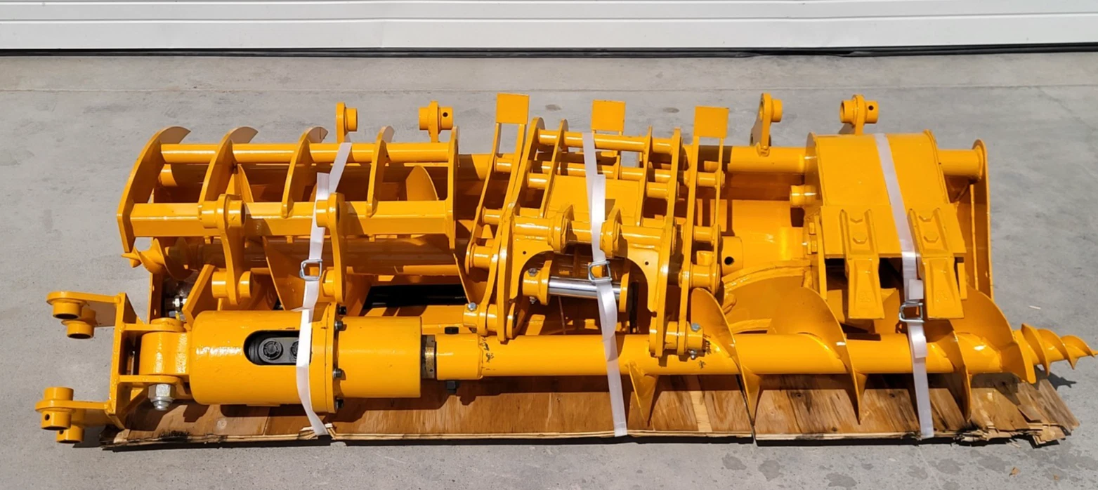 Yellow attachment package banded to a pallet: auger flighting, hydraulic cylinder, buckets and rake tines