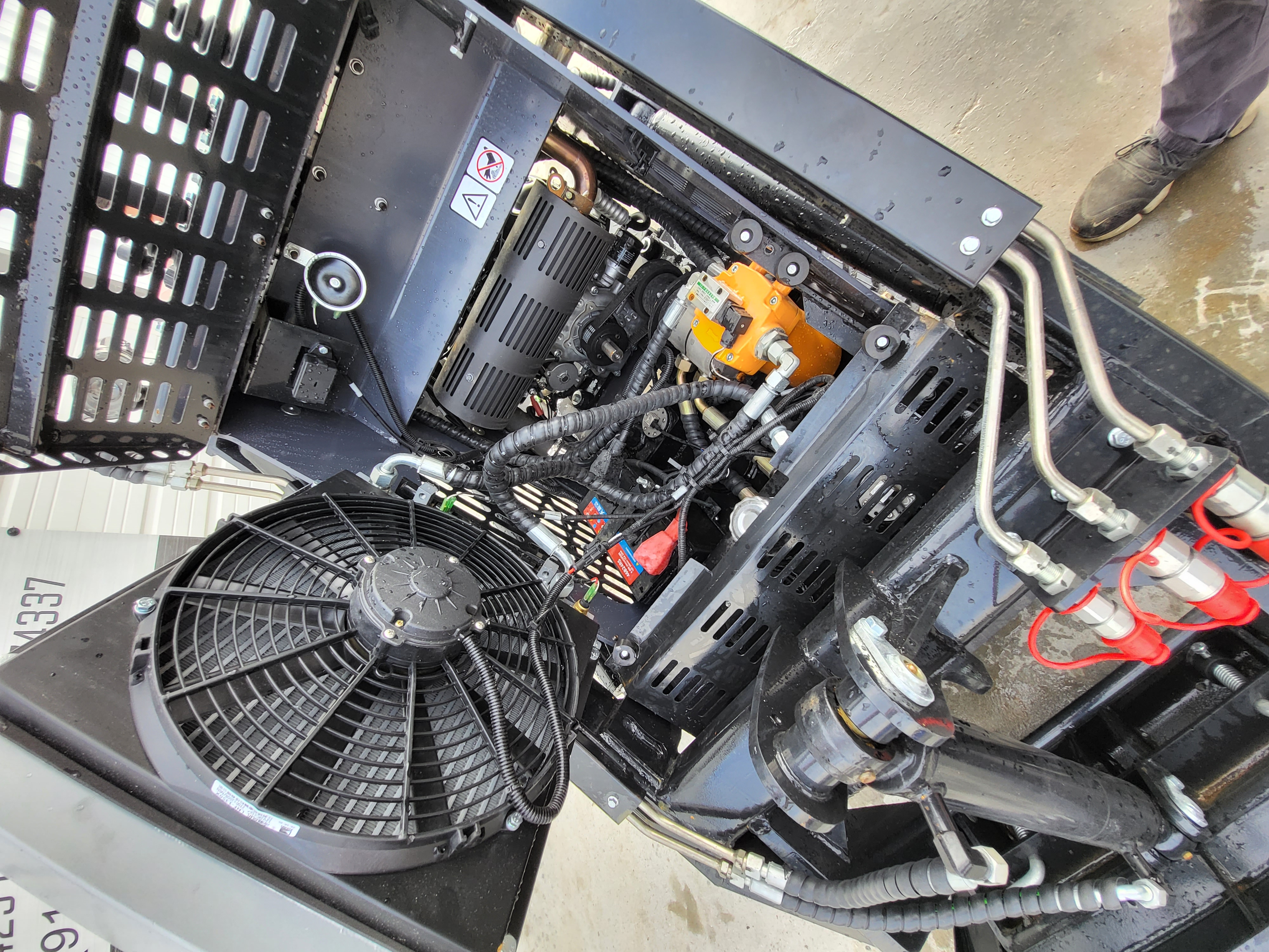 KRT23 engine bay open: electric cooling fan, hydraulic oil cooler and red-capped auxiliary quick couplers