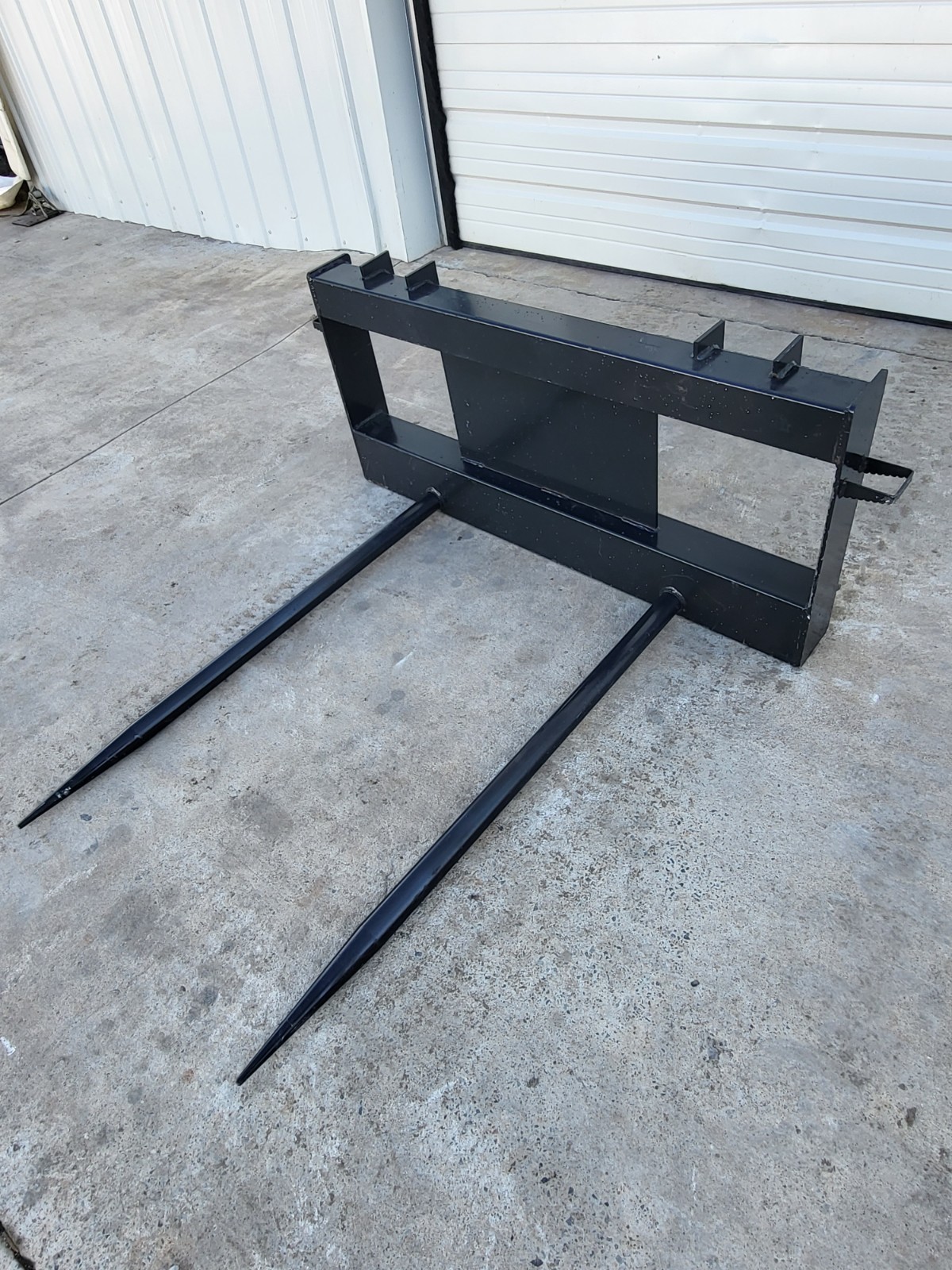 JCT double hay bale spear: black skid steer quick-attach frame with two long tapered tines pointing forward