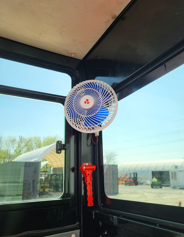 Mini excavator cab: 12-volt fan mounted on the door post beside a red emergency escape hammer