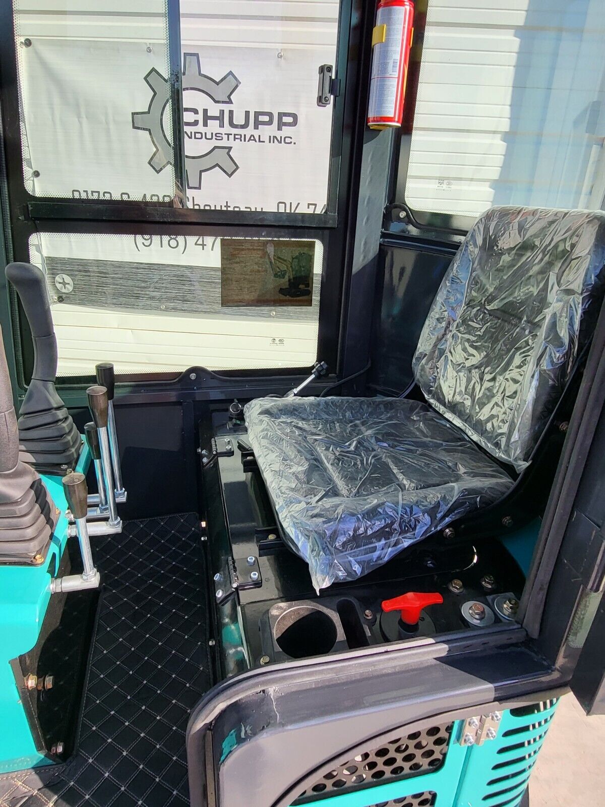 FF13 cab interior: plastic-wrapped operator seat, travel levers, red battery disconnect and a fire extinguisher