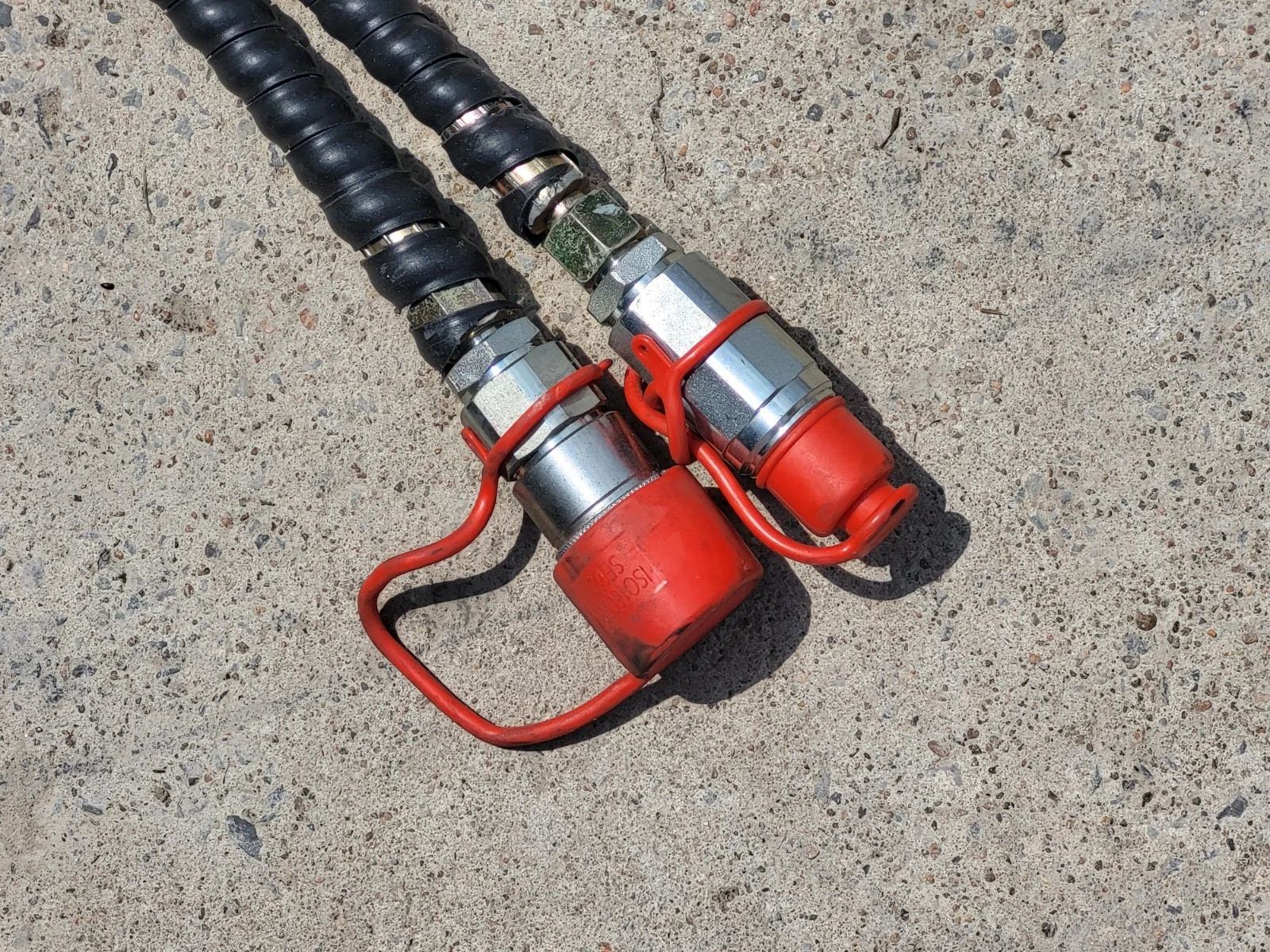 Two hydraulic hoses with red-capped flat-face quick couplers