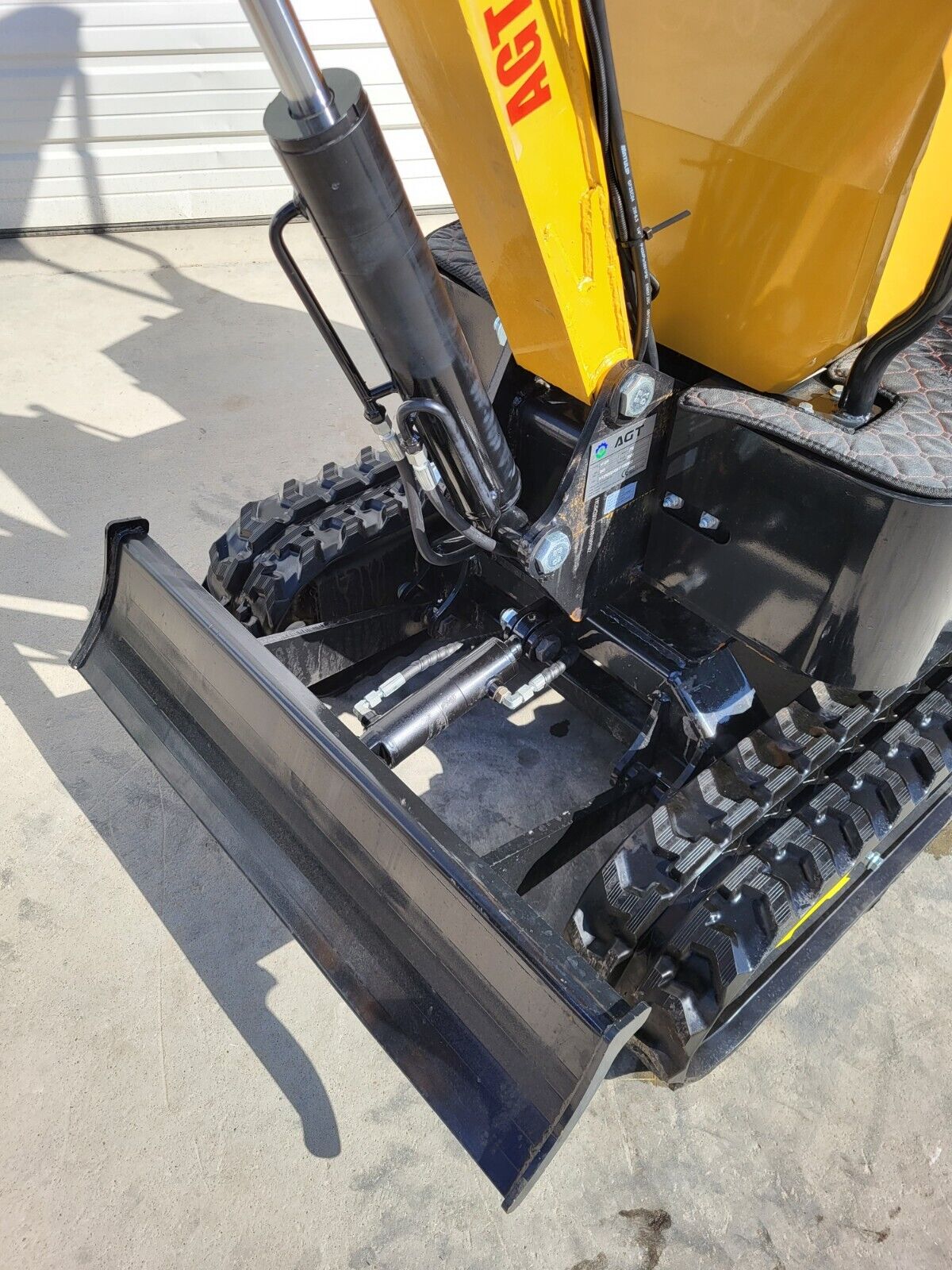Backfill blade and its hydraulic cylinder on the AGT H12R mini excavator, with the boom base and rubber tracks