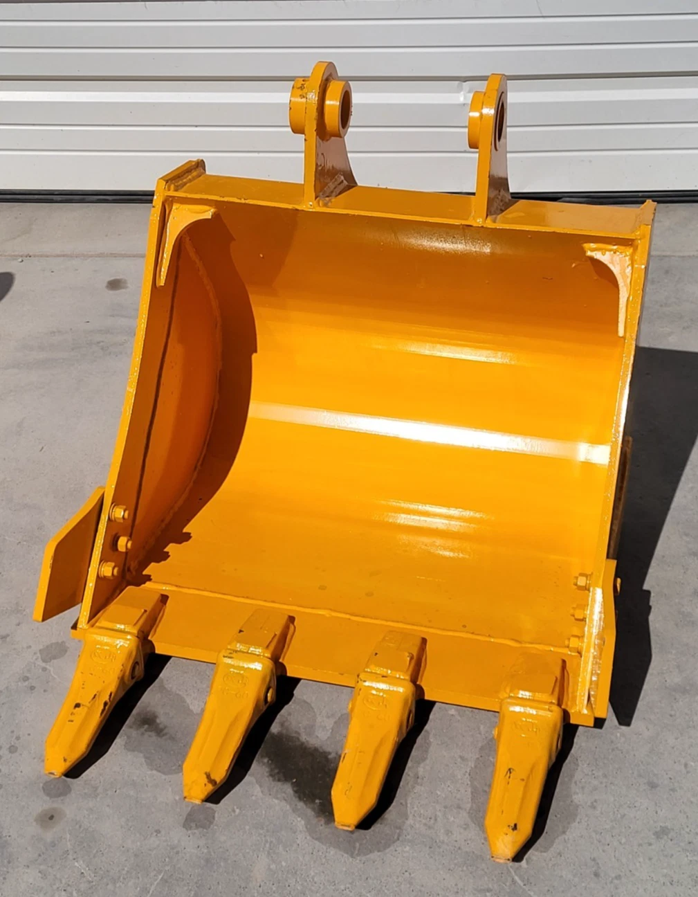 Yellow 24-inch excavator bucket standing open-face, four bolt-on teeth and twin pin-boss ears