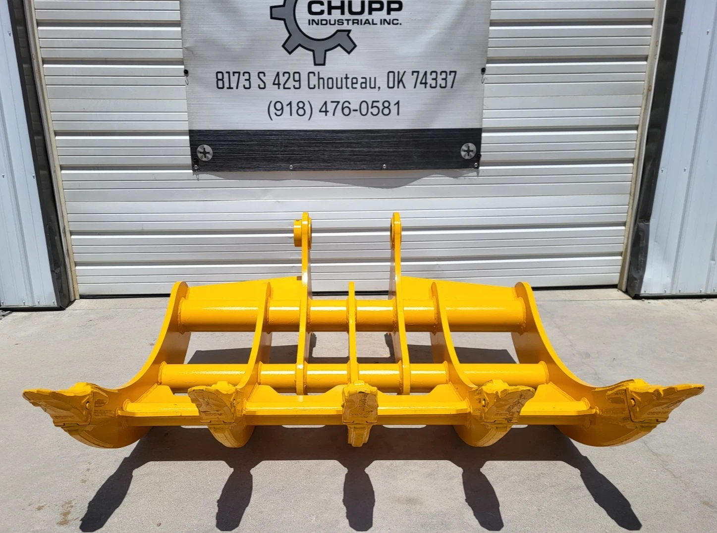 Yellow TOFT10R excavator rake front-on, five tine tips over a serrated bar, cross tubes and twin lugs