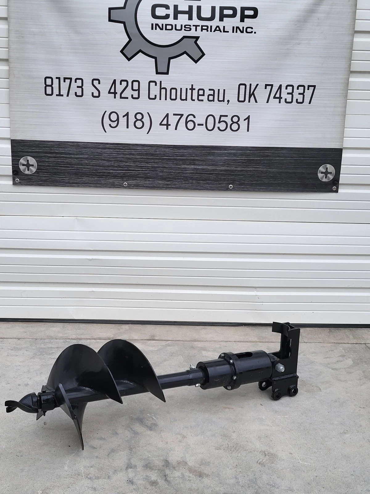 Black hydraulic auger with 16-inch bit below the Chupp Industrial shop banner