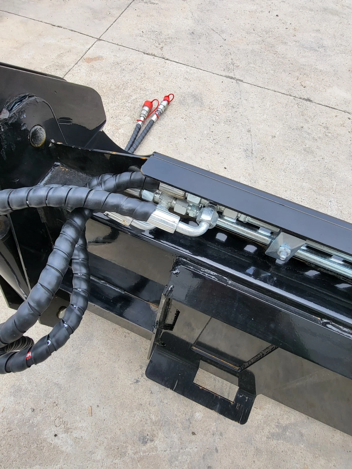 4-in-1 bucket quick-attach plate with sleeved hoses and red-capped hydraulic quick couplers