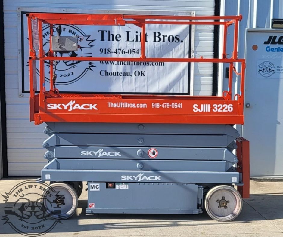 Orange SkyJack SJIII 3226 scissor lift, side view with the platform lowered, gray scissor stack and steel base