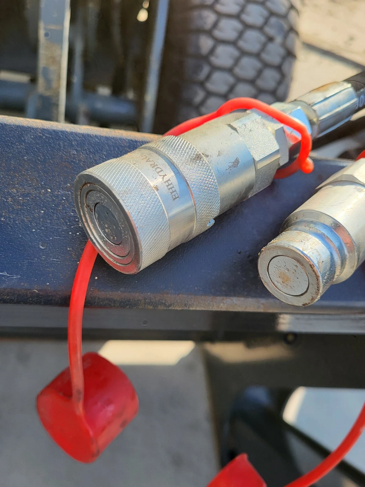 Hydraulic quick-connect couplers with red dust caps mounted on the log grapple crossbar