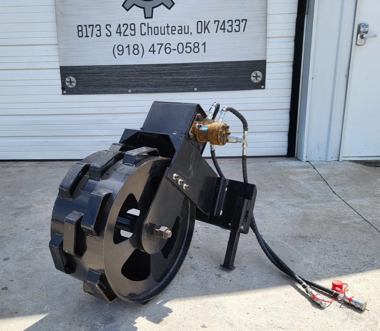 Trench compaction wheel on its park stand, welded cleats, hydraulic motor and red-capped hose couplers