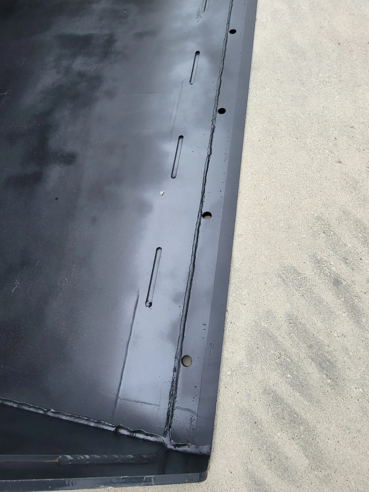 Bucket floor and side wall weld seam, row of bolt slots and holes along the cutting edge