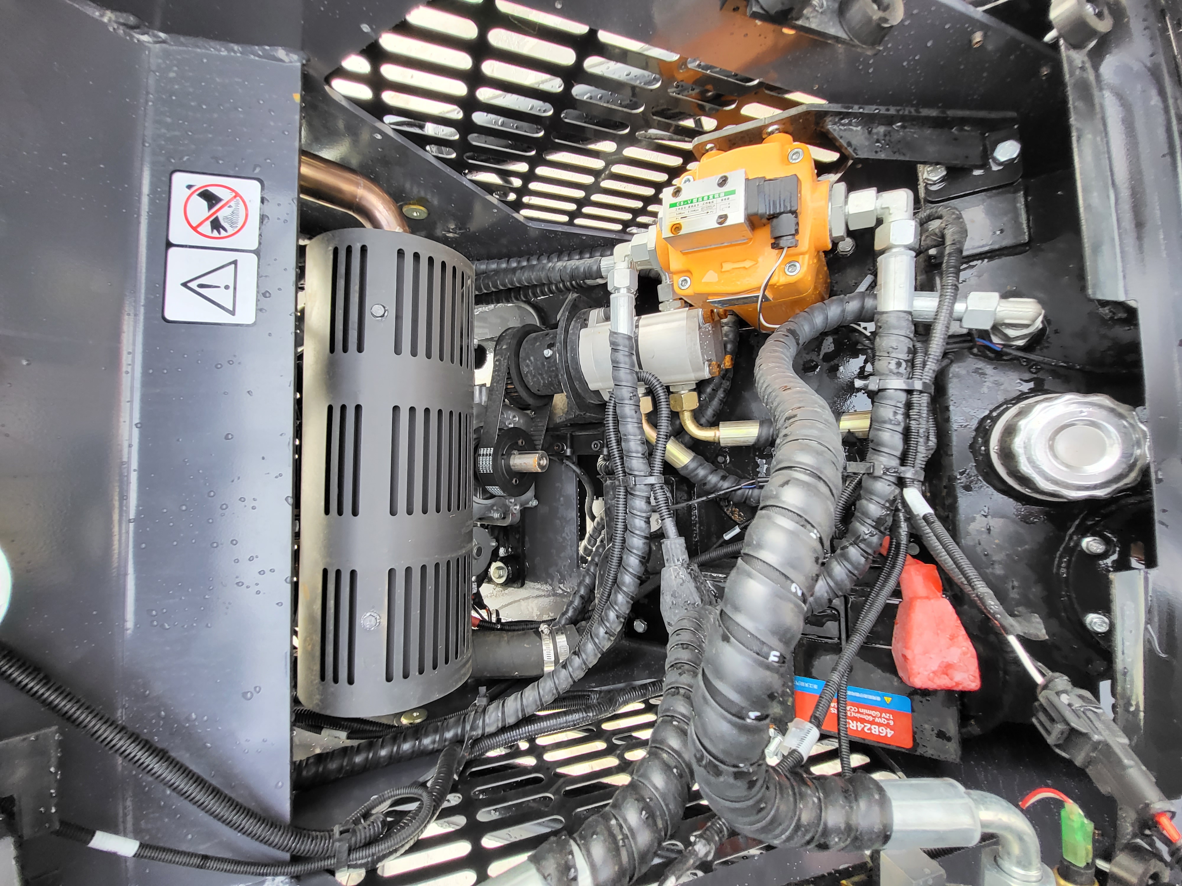 KRT23 hydraulic pump and drive belt behind the air cleaner, with braided hoses and the battery in the engine bay