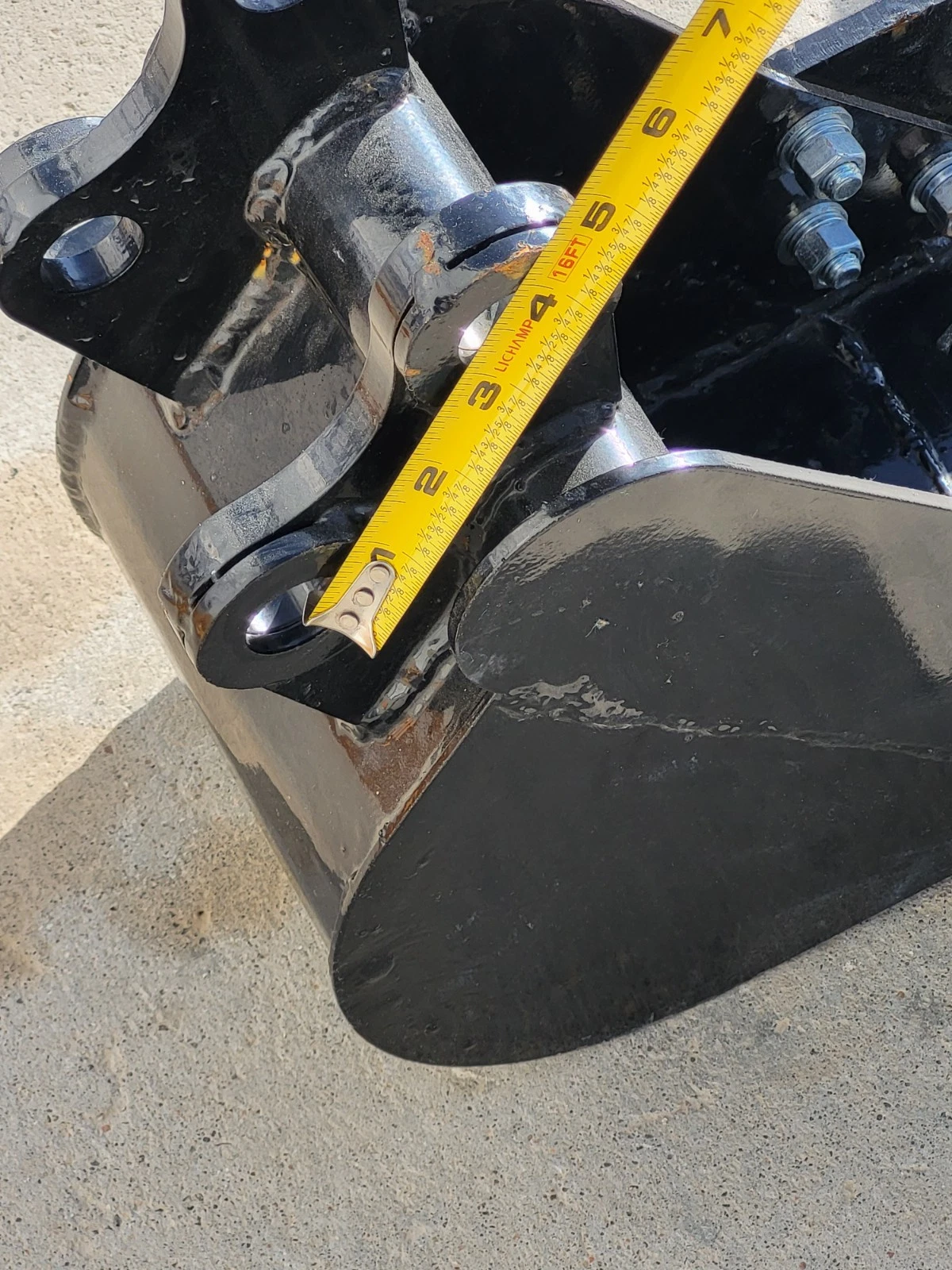 Tape measure along the trenching bucket's pin ears and boss, curved black side plate below