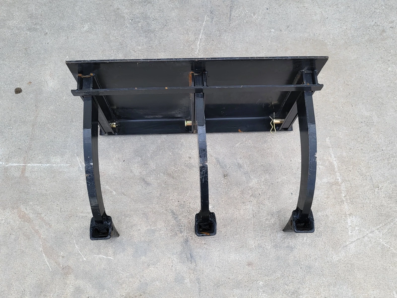 Three-tooth ripper from above: quick-attach mount plate and three curved steel shanks with boot tips