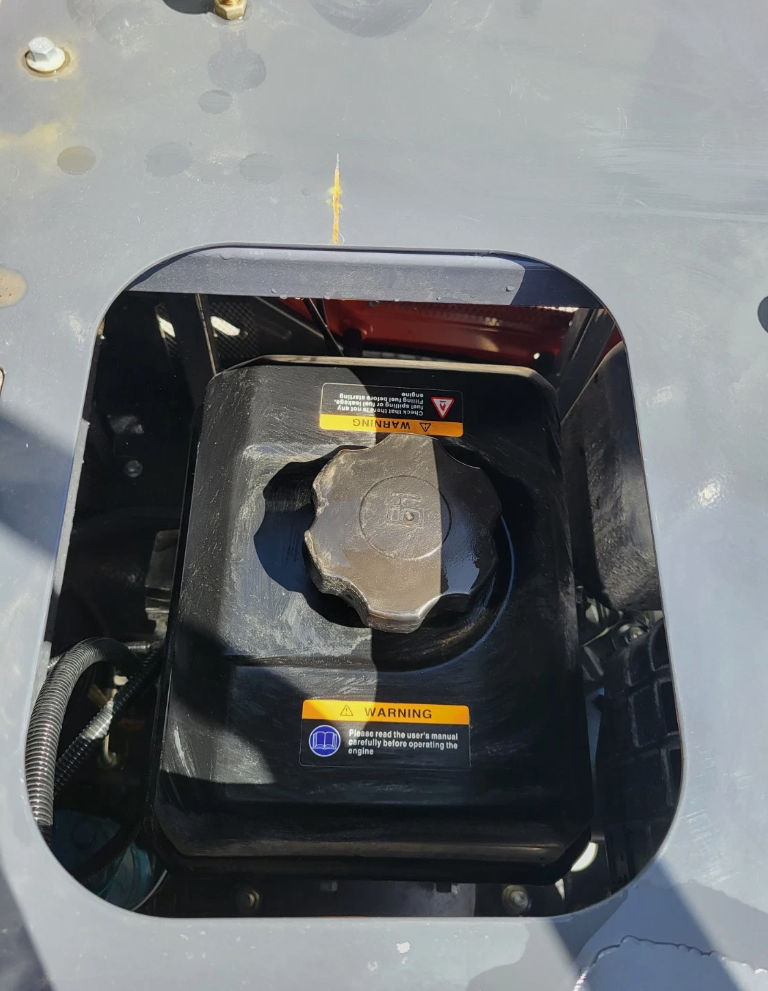 MX15R mini excavator fuel tank cap under the open deck hatch, with engine warning labels