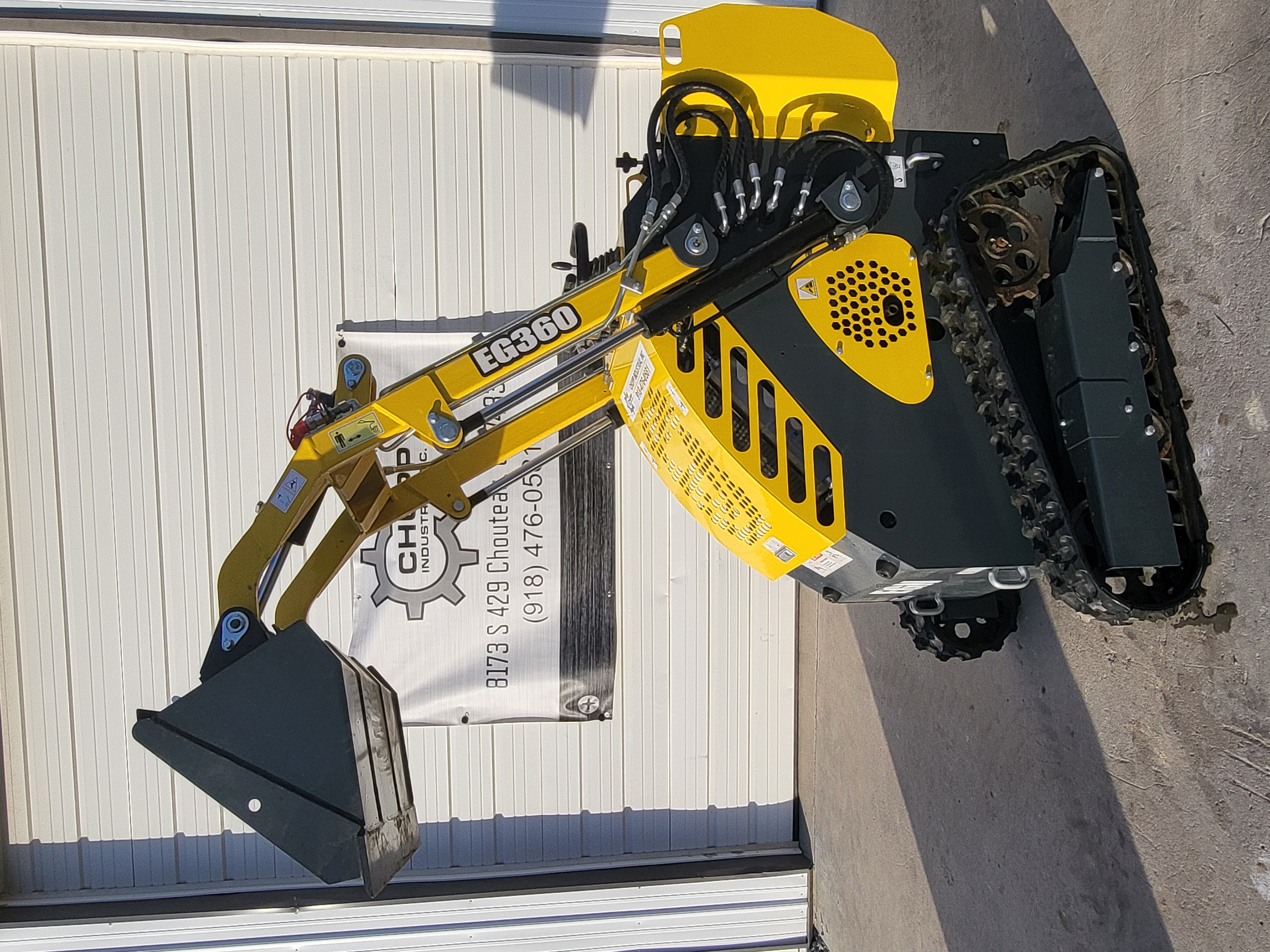 EG360 mini skid steer with the loader arms lifted and the bucket curled at full height above the rubber tracks