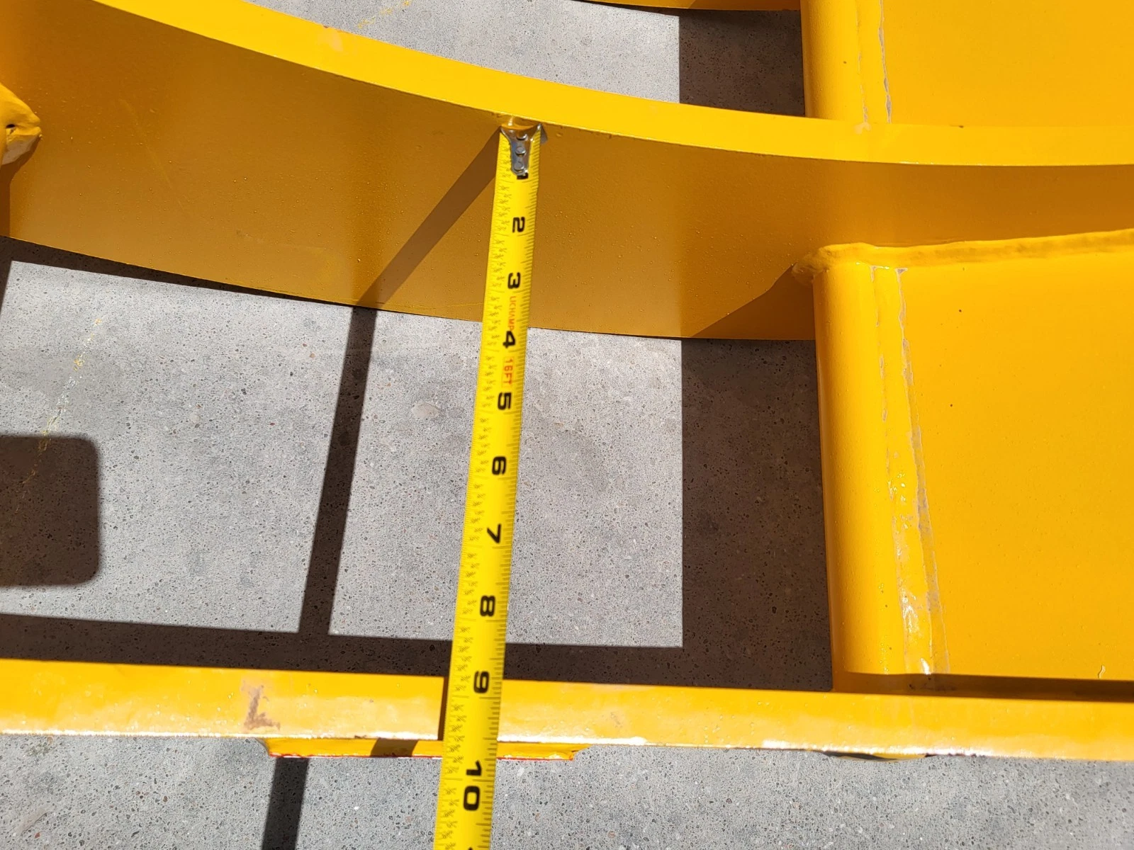 Tape measure spanning the gap between the yellow rake's curved frame bars, reading about 10 inches