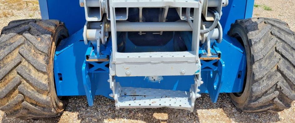 Blue scissor lift rear undercarriage: knobby rough-terrain tires, gray scissor-arm pivots and fold-down steel access steps