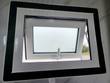Open hinged awning window, white frame with black trim, in a marble-look restroom wall