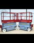 Two Skyjack scissor lifts side by side, lowered, red guardrail platforms on gray chassis with non-marking tires
