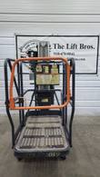 JLG 12SP push-around mast lift, lowered, end view of the platform with swing gate, mast and warning decals
