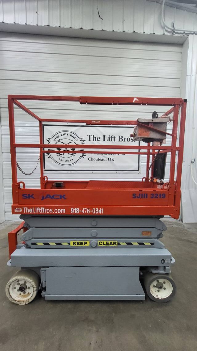 Orange and gray Skyjack SJIII 3219 scissor lift, fully lowered, side view with platform guardrails and control box