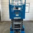 Genie GS-3232 scissor lift end view, blue platform with entry gate and ladder, stowed