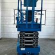 Genie GS-3232 scissor lift end view, blue platform rails over gray scissor stack, stowed