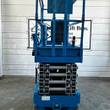 Genie GS-3232 scissor lift end view, blue platform rails over gray scissor stack, stowed