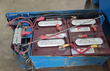 Battery tray on a blue Genie scissor lift: four red Trojan deep-cycle batteries, cables and charger