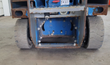 Rear of the Genie scissor lift: solid gray tires, blue drive motor housing and rusted steel frame