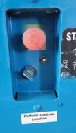 Recessed control panel on the blue lift: red emergency stop button, key switch and Platform Controls label